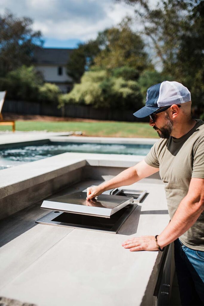 Chris Jones lifting outdoor kitchen stove top with an out of focus pool in the background