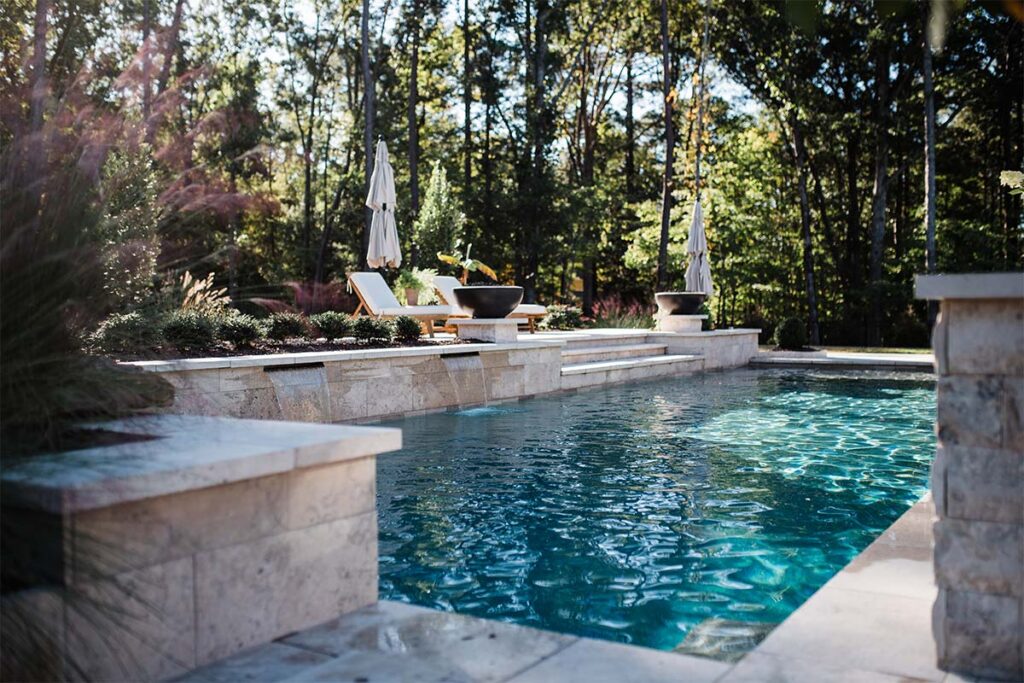 Wide ground view of contemporary Raleigh project showcasing wall water falls, patio leading into pool and pool surrounds