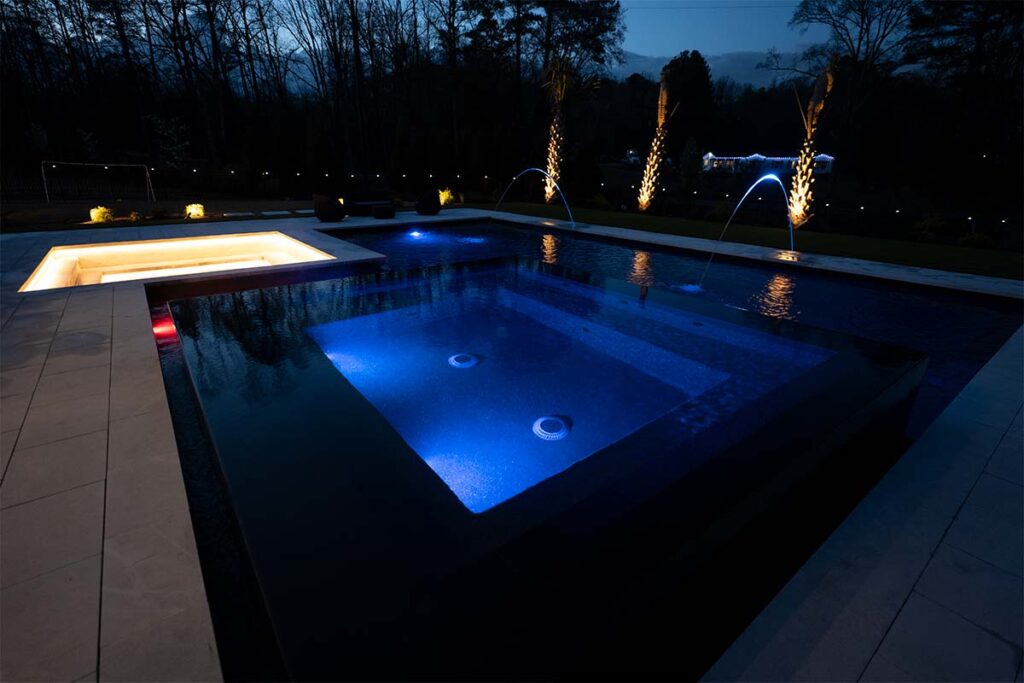 Close up of Modern Apex at night showcasing pool lighting, outdoor lighting, and black mirror spa