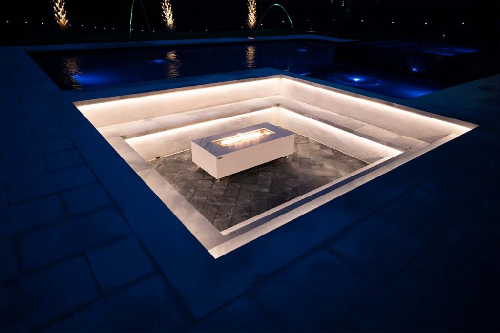 Modern Apex concrete pool at night with sunken fire pit lounge in focus, through use of outdoor lighting and active fire pit