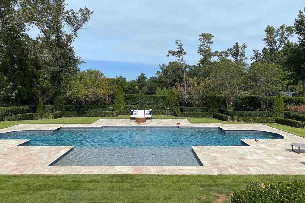 Wide view of custom shape concrete pool, Classic Costal, with ledge for pool loungers